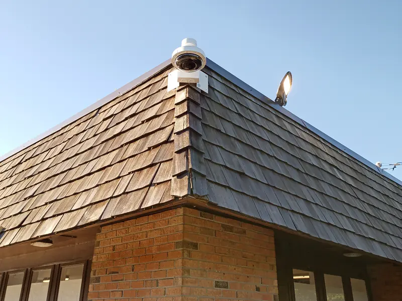 Camera on a pendant mount at the corner of a shingled roof.