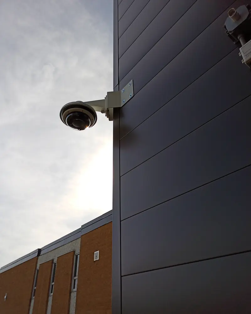 Multi-sensor camera on a wall arm against dark metal cladding.