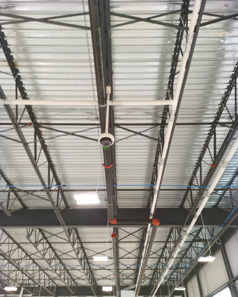 Camera on a conduit drop from the roof trusses of a warehouse.