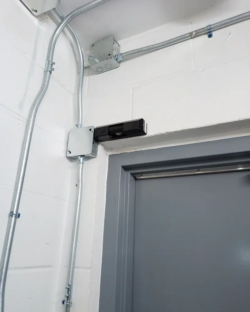 Conduit and a junction box above a door, feeding the lock at the head of the frame.