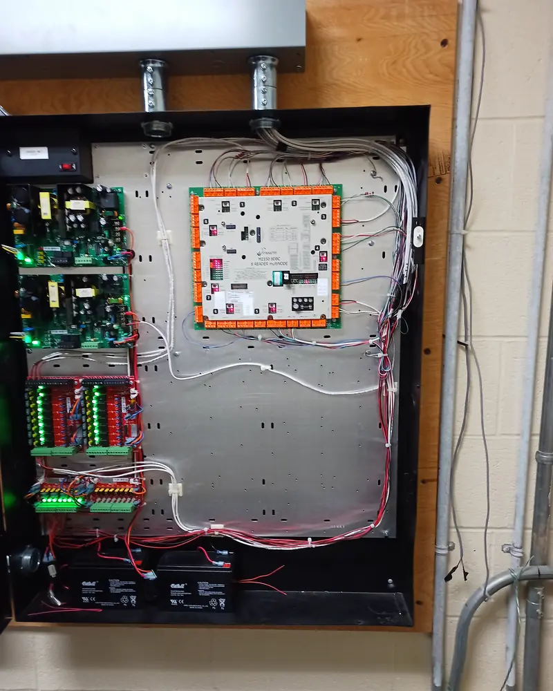 Open enclosure with a door controller, power supplies, output boards and two batteries, status lights on.