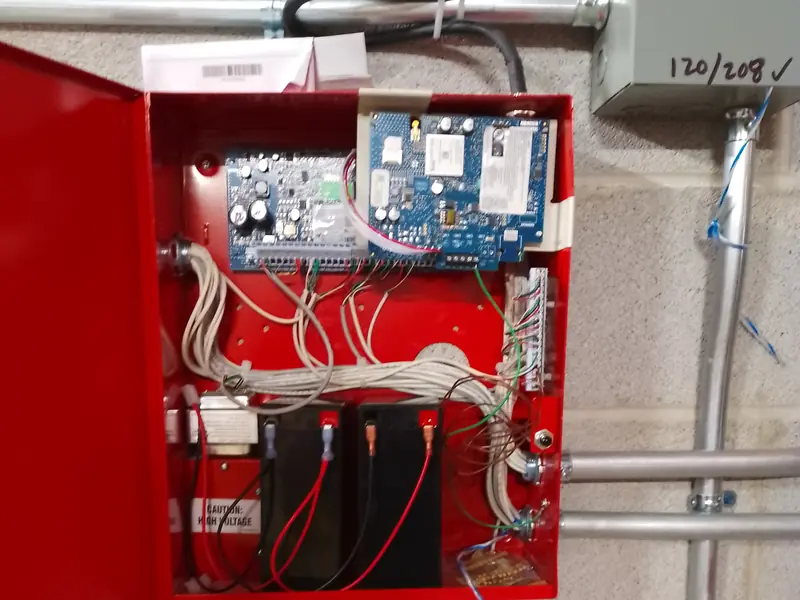 Open red enclosure with two circuit boards, dressed wiring and two batteries.