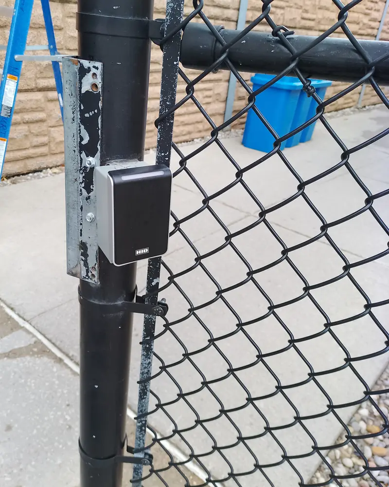 Card reader on the post of a chain-link pedestrian gate.