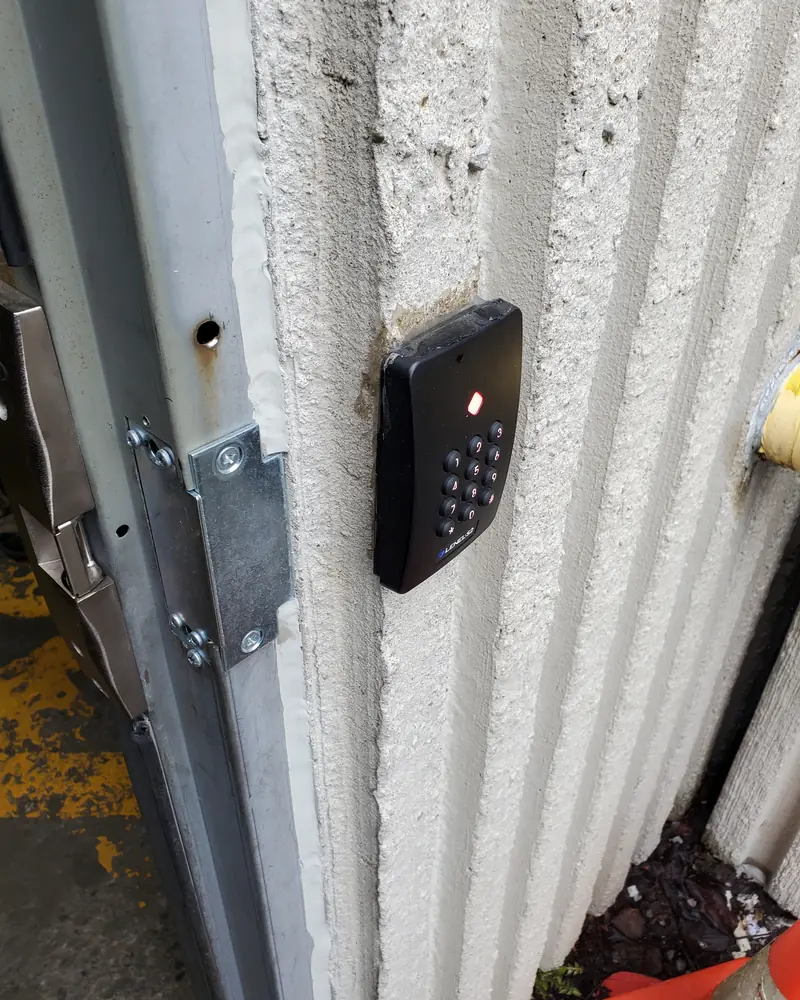 Keypad reader on a ribbed concrete wall beside a steel door frame.